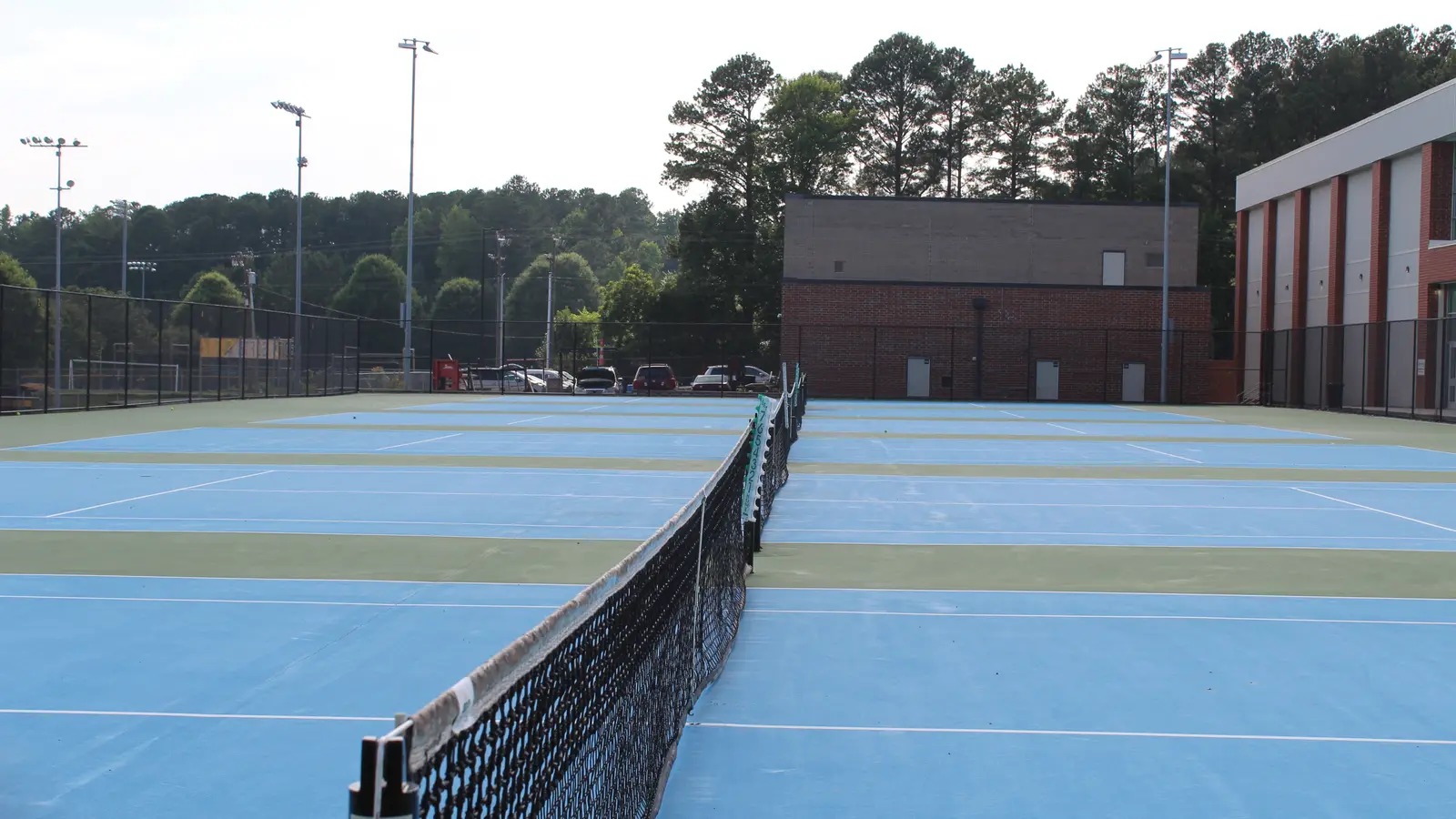 Pistas de tenis vacías al aire libre, con árboles al fondo.